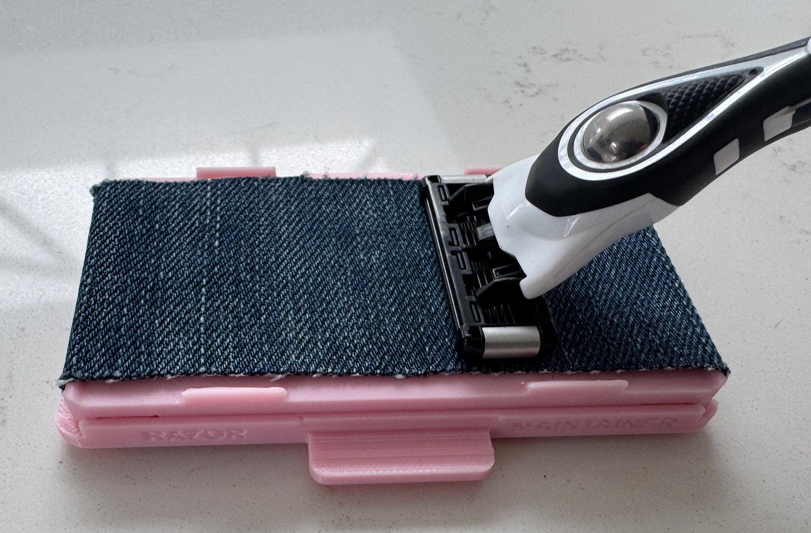 Razor cartridge resting on the Blush Pink Razor Maintainer's recycled denim stropping strip